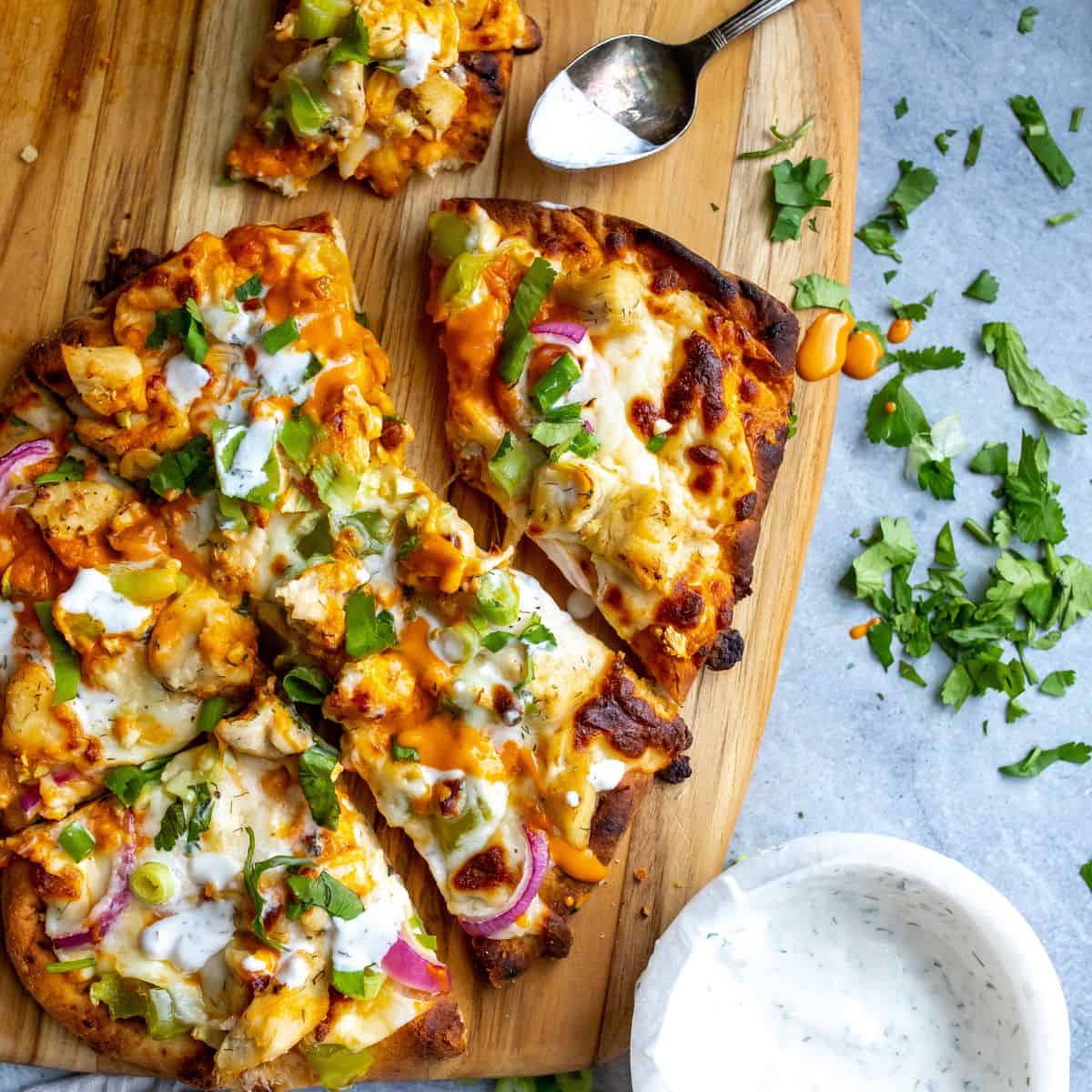 Buffalo chicken flatbread on a cutting board with ranch on the side. 