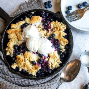 Black skillet with blueberry cobbler, ice cream and a silver spoon.