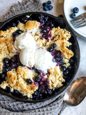 Black skillet with blueberry cobbler, ice cream and a silver spoon.