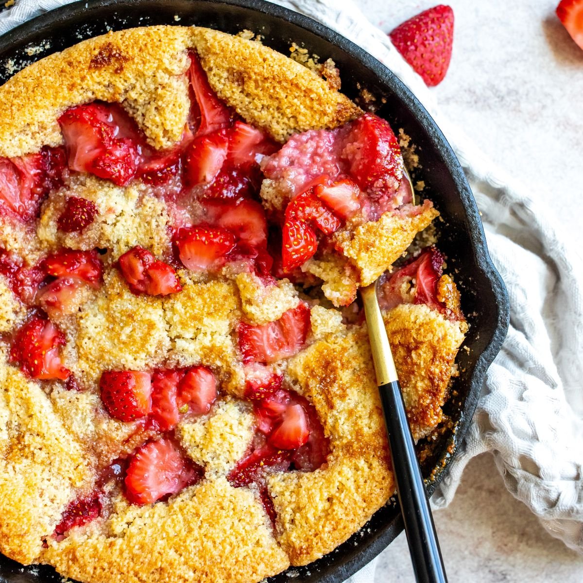 Strawberry cobbler in a cast iron with a spoon and fresh strawberries. 