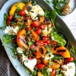 Grilled peach burrata salad on greens in a serving platter.