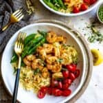 White bowl with gold fork and lemon pepper shrimp and toppings.