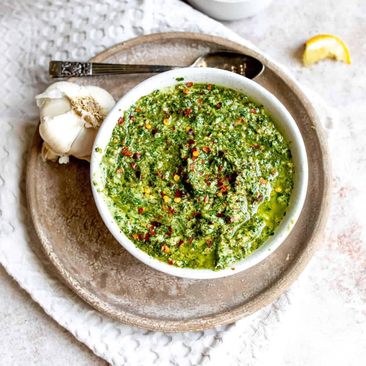White bowl with pesto and a silver spoon on the side. 