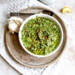 White bowl with pesto and garlic on the side with a silver spoon.