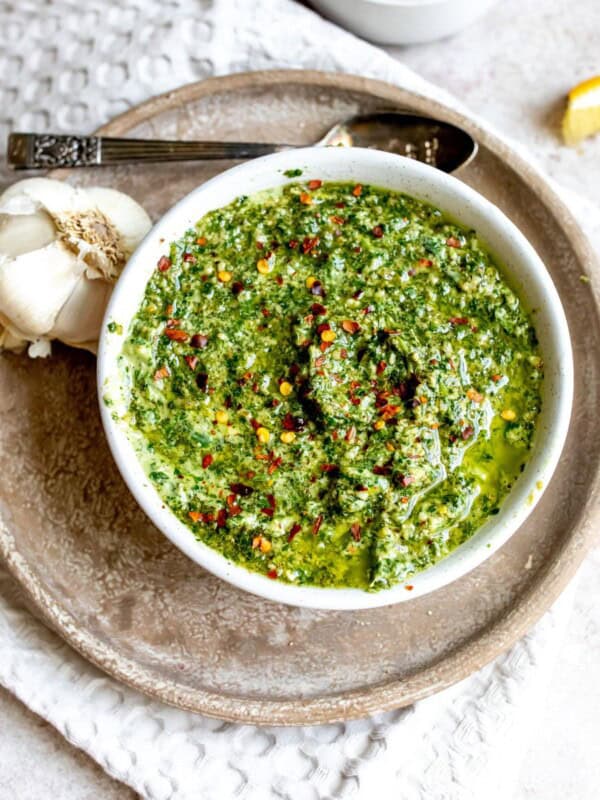 White bowl with pesto and garlic on the side with a silver spoon.