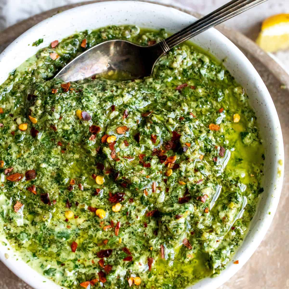White bowl with fresh pesto and a small silver spoon in the sauce. 