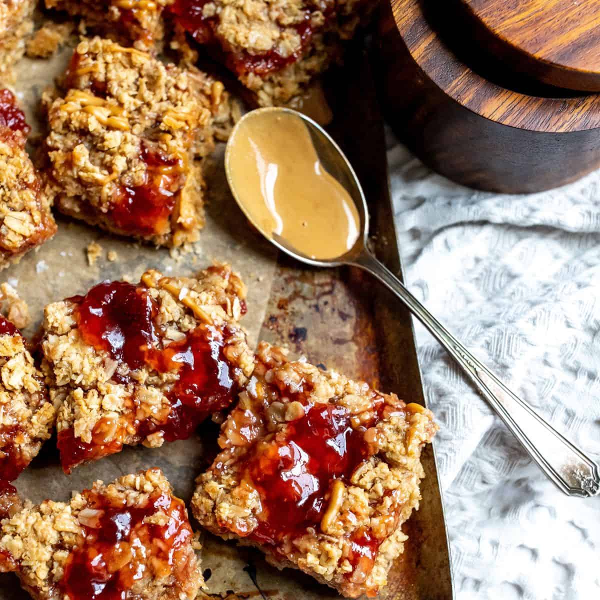 Peanut butter jelly bars with a silver spoon full of peanut butter next to them. 