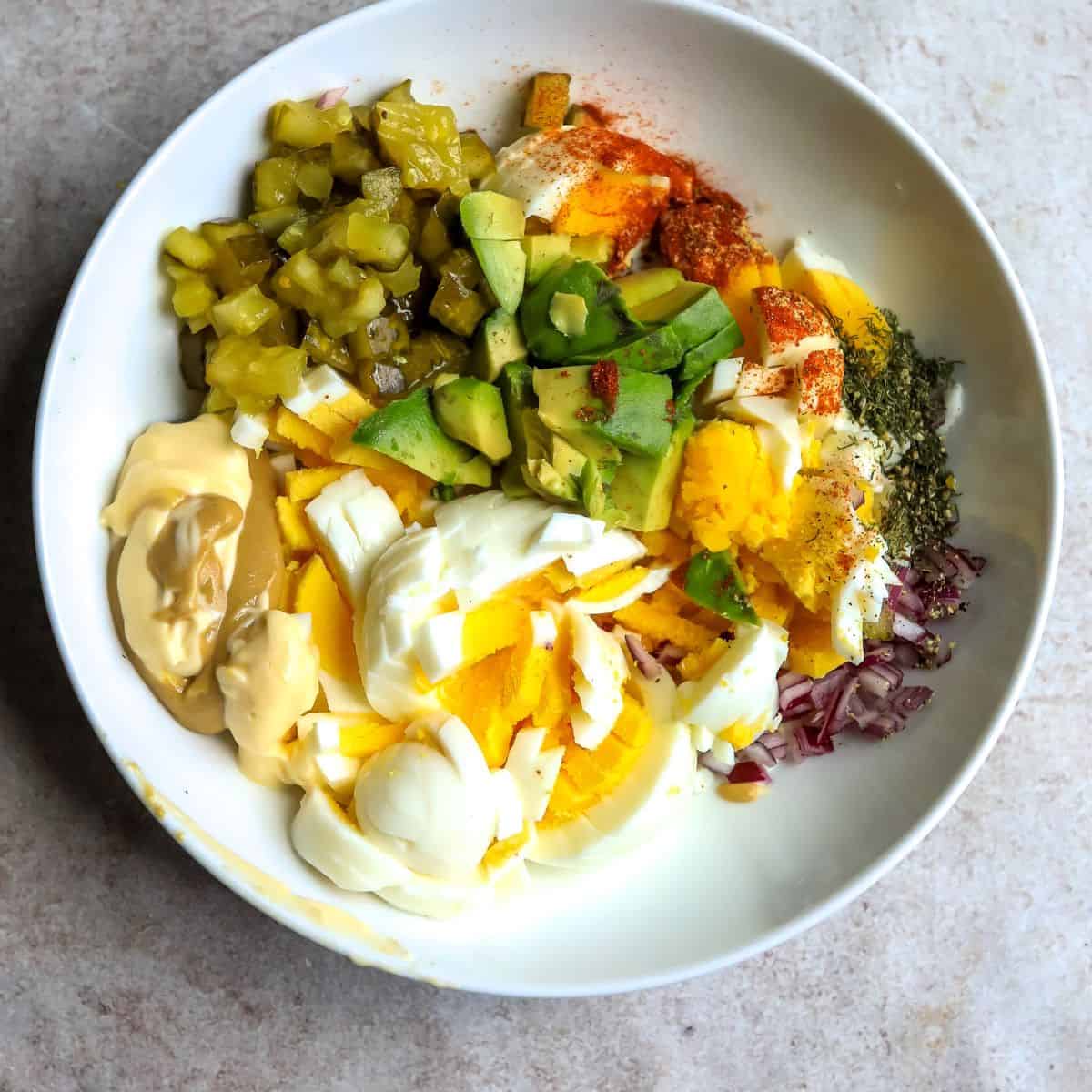 White bowl with ingredients in it to make avocado egg salad. 