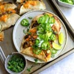 Crispy Black Bean Tacos on a white plate with limes and cilantro, sour cream and jalapeño.
