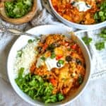 White ceramic bowls with slow cooker chicken enchiladas and lettuce, a silver fork on the side.