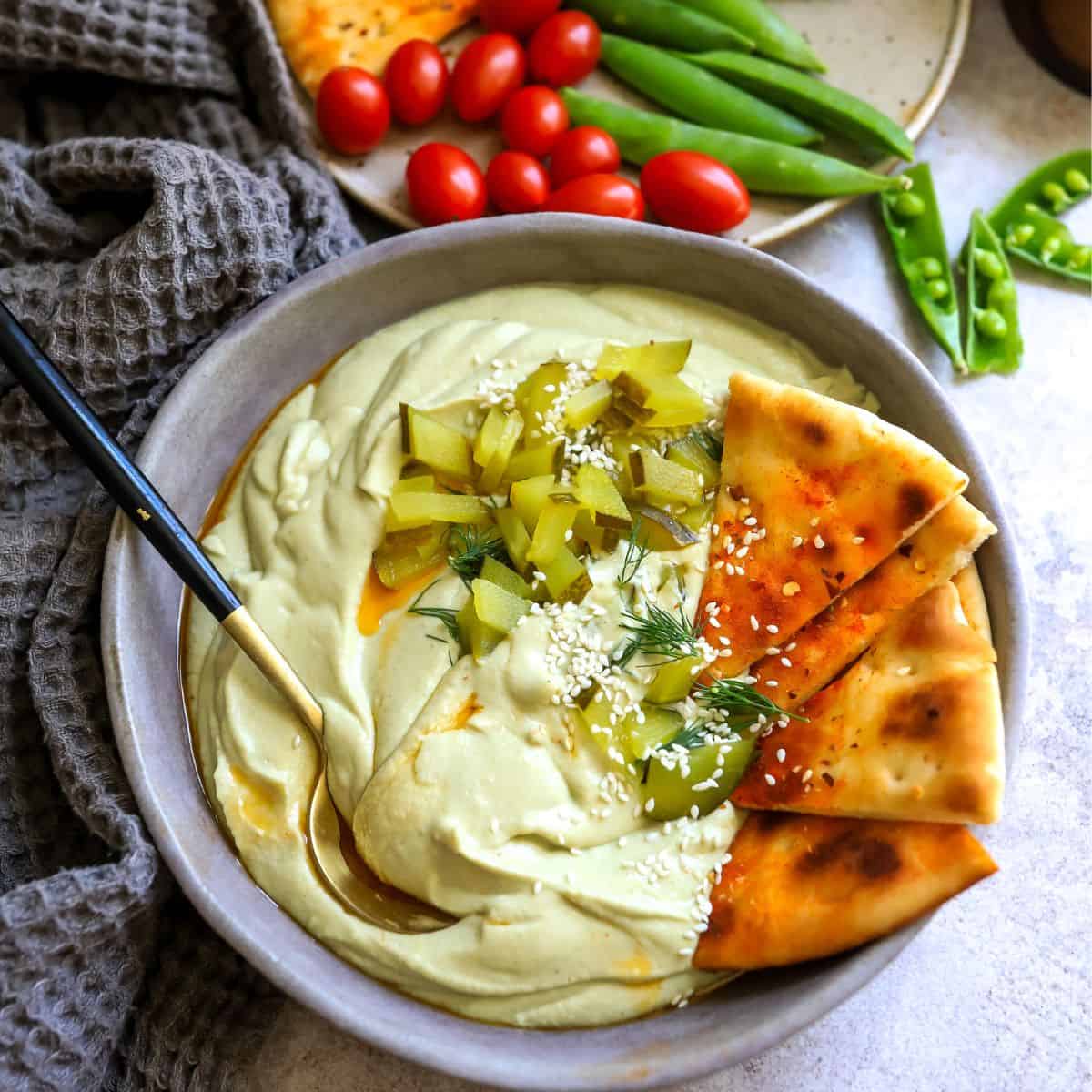 Hummus and pickles dip in a bowl with toasted pita. 