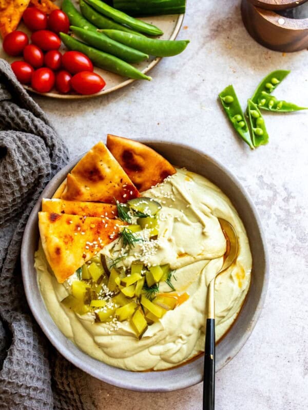 Dill pickle hummus in a gray bowl with a spoon in it and veggies on the side.