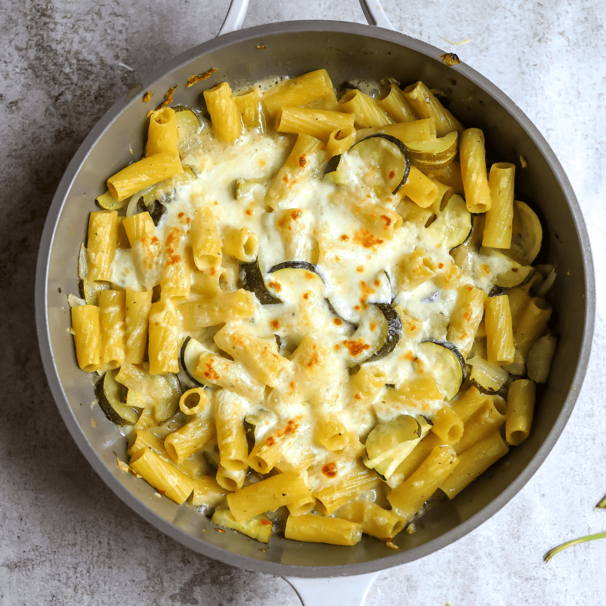 Grey skillet with melted cheese over lemon noodles. 