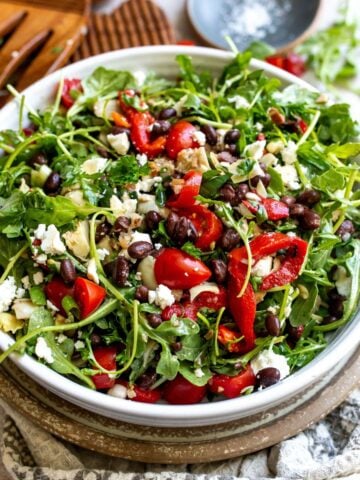 Mediterranean Black Bean Salad in a ceramic white bowl with salad serving utensils.