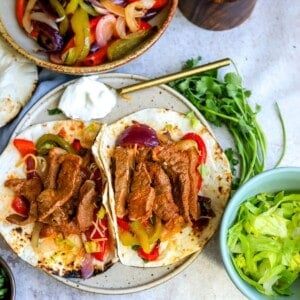 Shrimp and steak fajitas on a ceramic plate with sides and sour cream.