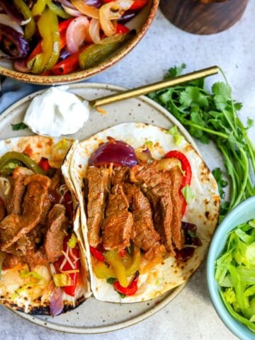 Shrimp and steak fajitas on a ceramic plate with sides and sour cream.