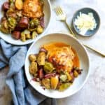 Two white ceramic bowls with chicken, veggies and potatoes in them.