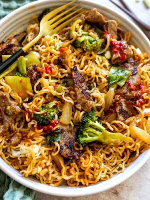 White bowl with noodles and crispy beef in it. Red sauce and a fork.