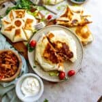 Tortillas stuffed with chicken and toppings on a ceramic plate with a fork on the side.