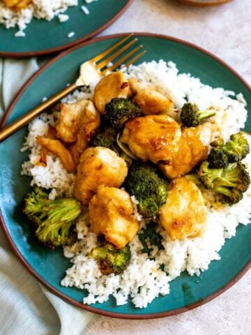 Green plate with rice and chicken and broccoli. Gold fork in the chicken.