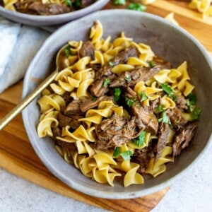 Grey bowls with noodles and beef. A gold spoon on the side with parsley garnish.