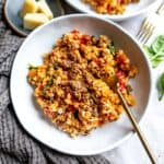 White ceramic bowl with risotto and tomatoes and a gold fork on the side.