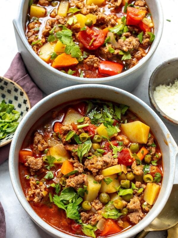 Two bowls of slow cooker hamburger soup with sausage and potatoes on a countertop for serving.