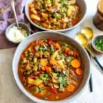 Grey bowls with soup, burger and veggies in it. Gold spoons on the side and parsley.