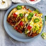Beef soft tacos on a gray plate with cheese, lettuce, and jalapenos.