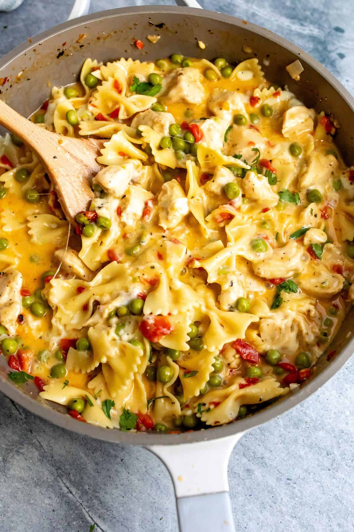 Large grey skillet with cheesy pasta and hunks of chicken in it. 