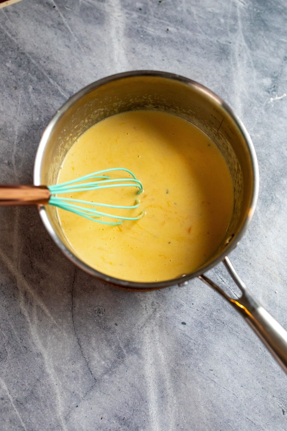Stainless Steel pot with melted cheese sauce in it and whisk. 