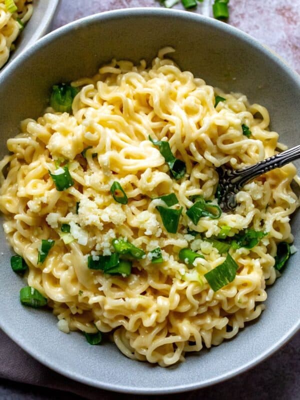 Grey ceramic bowl with green onions and cheesy ramen.