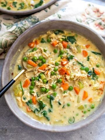Grey bowls with creamy soup and veggies in it, a gold and black spoon.