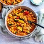 Grey bowls with soup in them, noodles and chicken. Gold spoons to the side.