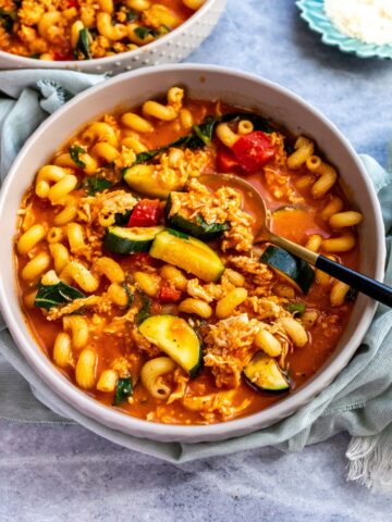 Grey bowls with soup in them, noodles and chicken. Gold spoons to the side.