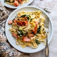 White ceramic plate with pasta, cream sauce and salmon. A silver fork on the side.