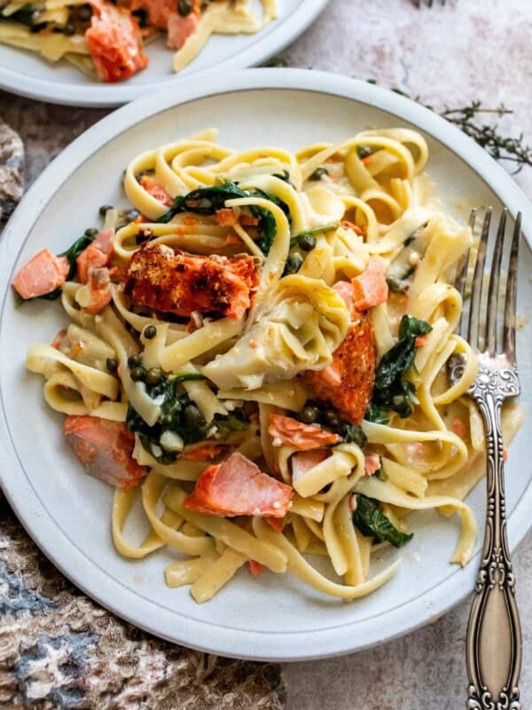 White ceramic plate with pasta, cream sauce and salmon. A silver fork on the side.