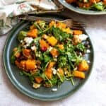 Green plate with salad and roasted butternut squash on it. Silver fork on the side.