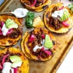 Sheet pan with shredded beef tacos topped with avocado, pickled onions, and sour cream.