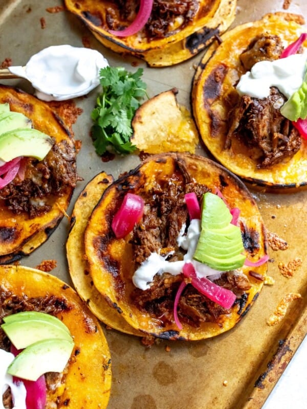 Sheet pan with shredded beef tacos topped with avocado, pickled onions, and sour cream.