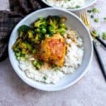 White ceramic bowls with rice and cooked chicken and green onions for garnish. Gold forks on the side.