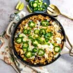 Skillet filled with chicken and cheese and jalapeños on top. Gold serving spoon on the side.