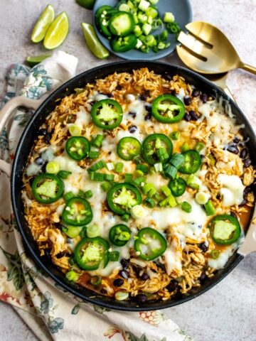 Skillet filled with chicken and cheese and jalapeños on top. Gold serving spoon on the side.