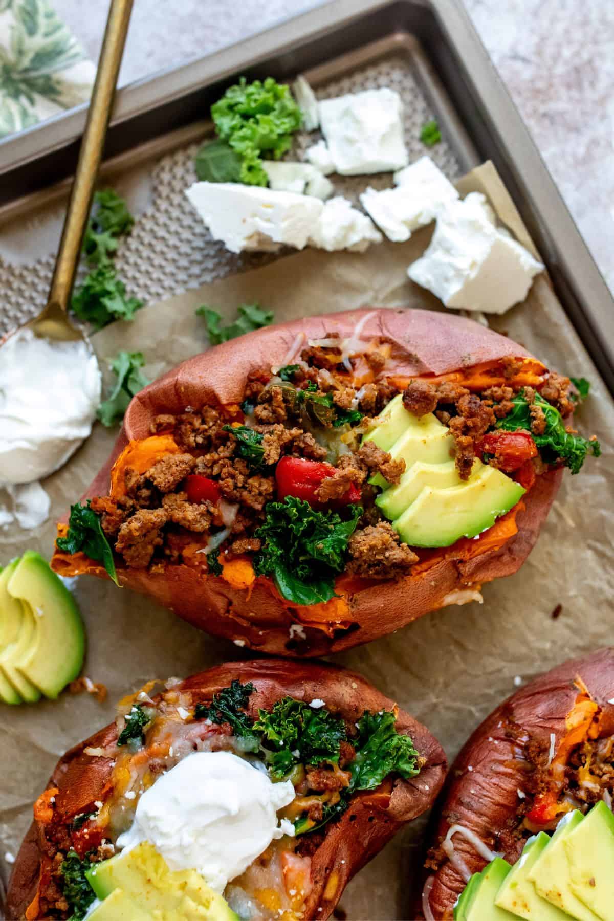 Baking sheet with parchment paper and sweet potatoes loaded in toppings. 