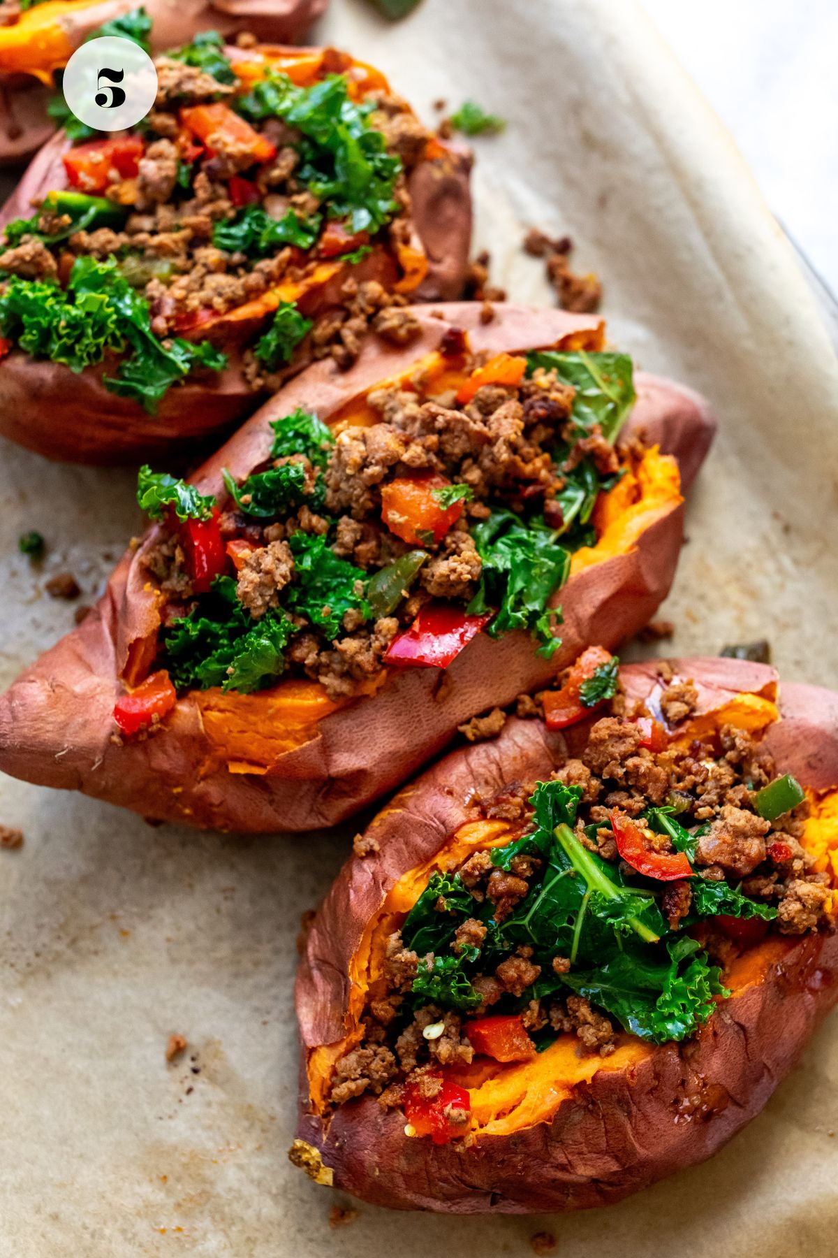 Close up photo of sweet potatoes on a baking sheet stuffed with ground beef. 