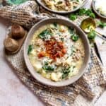 Grey pottery bowls filled with creamy soup and crispy bacon on top. Garnished with parsley and a gold spoon.