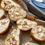 Pears on brown parchment paper with almonds on top. Honey on the side with plates.