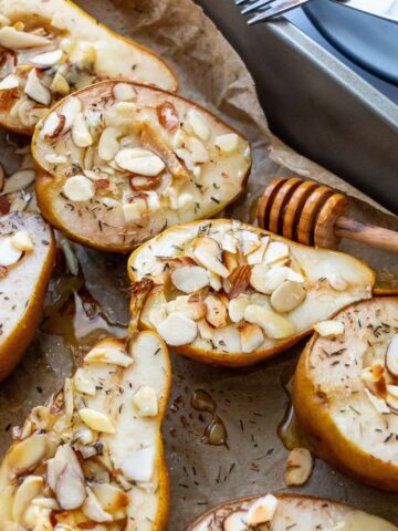 Pears on brown parchment paper with almonds on top. Honey on the side with plates.