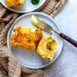 Small white plate with cornbread on it and jalapeños. A butter knife with butter on it.