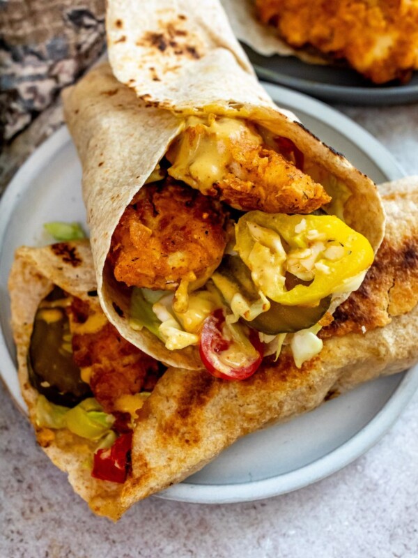 Chicken wraps with honey mustard on a white plate with pickles.